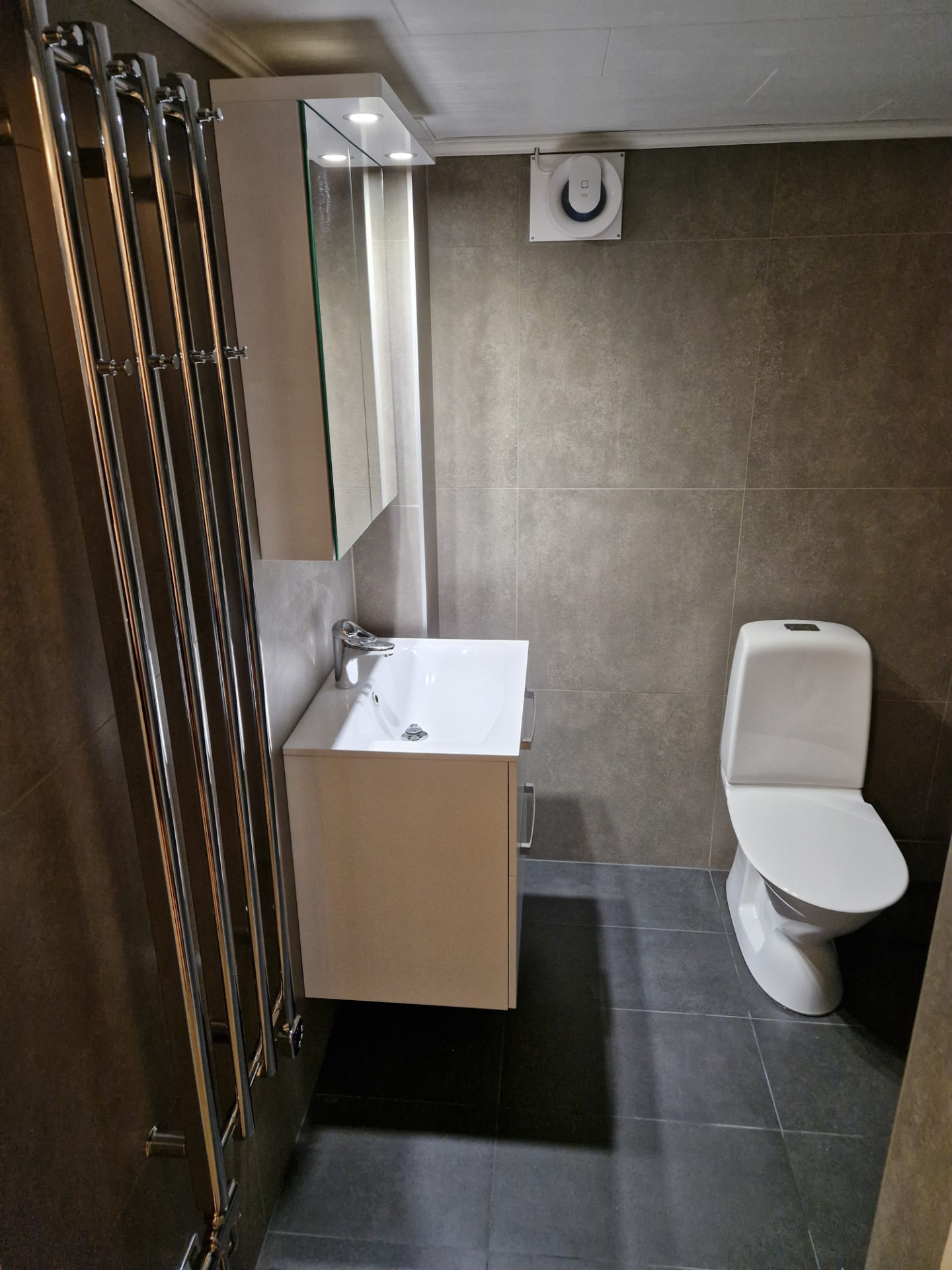 Renoverat badrum med grått kakel, kommod och toalett