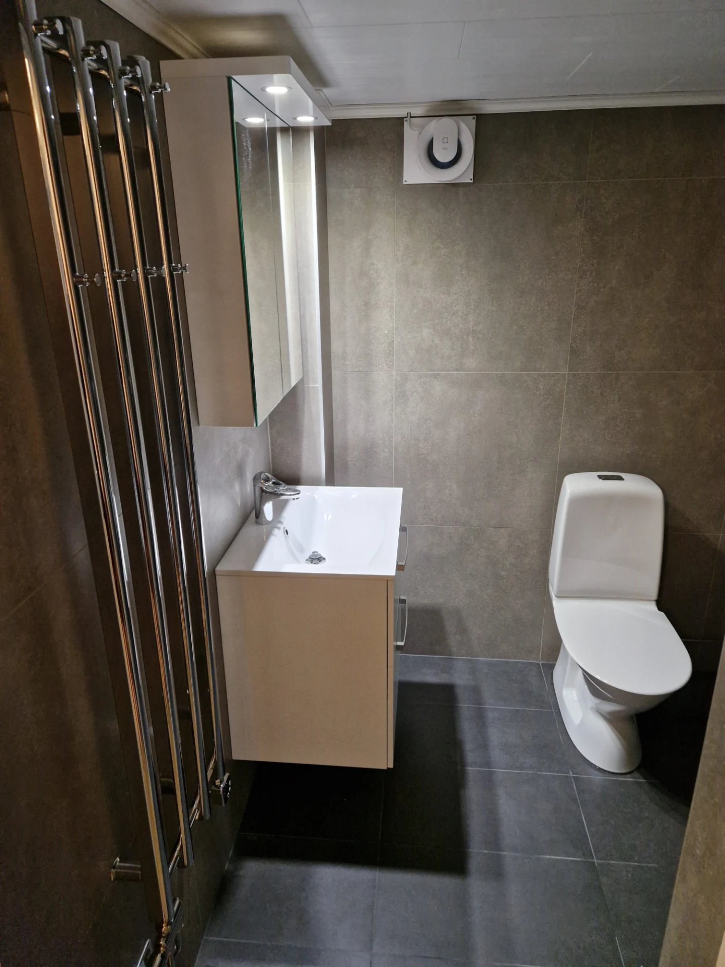 Renoverat badrum med grått kakel, kommod och toalett